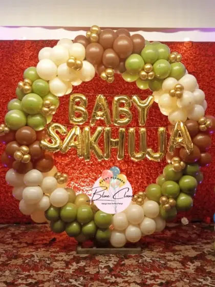 A baby shower decoration with a balloon ring in earthy tones of green and brown, with the family name in foil letters.