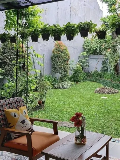 A comfortable patio setup with a view of the backyard. The space is perfect for relaxing, with a wooden armchair and a small table, surrounded by hanging plants and a well-maintained lawn.
