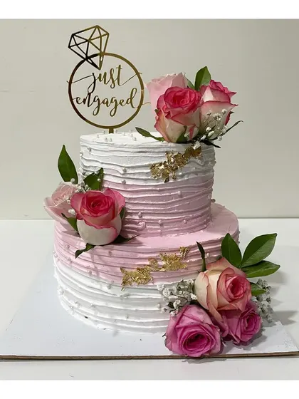A classic and elegant two-tier engagement cake. This 3kg cake features a textured pink and white ombre design, decorated with fresh roses and a "Just Engaged" topper.