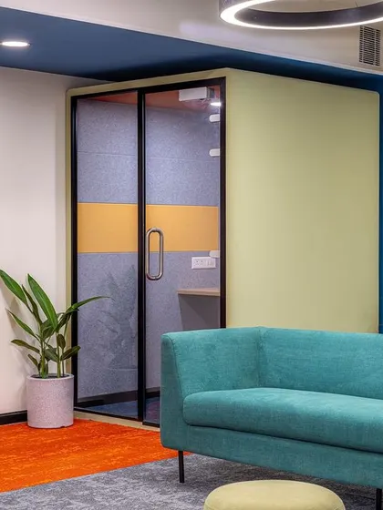 A vibrant acoustic pod adds a pop of color and high functionality to this breakout area. It provides a soundproof space for private calls without having to leave the collaborative zone.