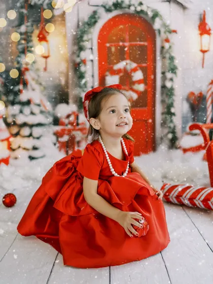 A little girl in a beautiful red dress, looking up at the magic of the Christmas setup.