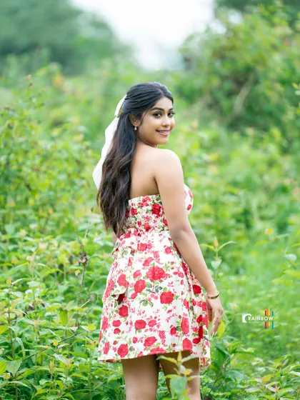 A back view of a model in a floral dress, walking through a green field.