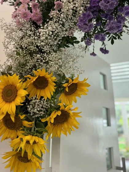A close-up of the sunflower arch over the doorway, showing the lush combination of yellow sunflowers, white baby's breath, and purple statice.