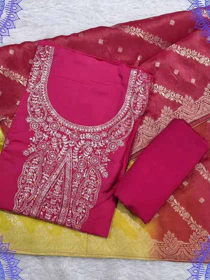 A bright and cheerful dress material set with a pink top and a yellow and red Banarasi dupatta. The intricate embroidery on the top adds a festive touch.