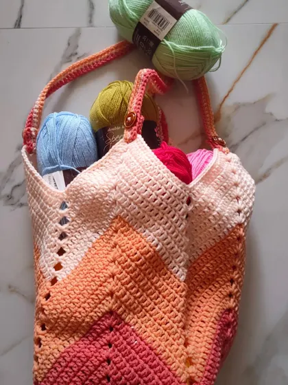 Another look at the Chevron Tulip Bag, showcasing its unique V-shape opening and how easily it holds multiple skeins of yarn. The warm, peachy tones are created with a lovely worsted weight acrylic yarn.