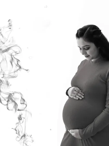 A serene and artistic black and white portrait. The mom-to-be looks down at her bump, with a wisp of smoke-like effect adding a creative and ethereal touch to the image.