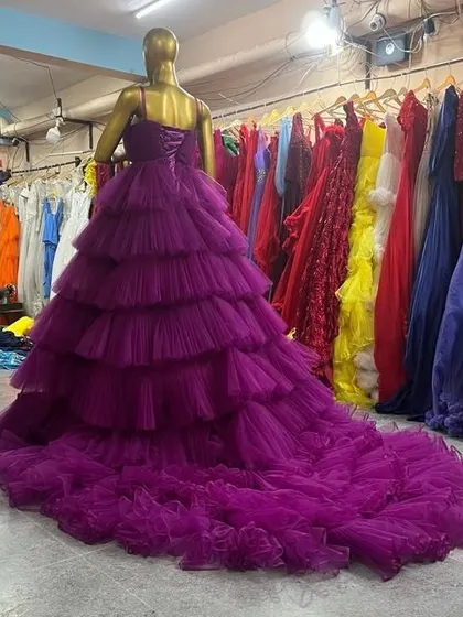 A back view of a stunning purple gown with a fully tiered and ruffled skirt and a long train. The corset back ensures a customizable and comfortable fit.