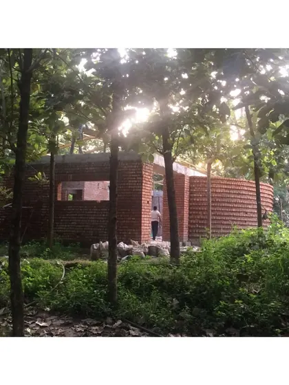 A work-in-progress shot of the Pasumandha residence, nestled within a grove of trees. The curved brick wall is designed to harmonize with the natural surroundings, creating a structure that feels like it grew from the site itself.