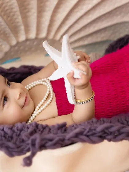 A dreamy close-up of the baby girl in her seashell bed, holding a starfish. These detailed shots add a magical touch to the collection.