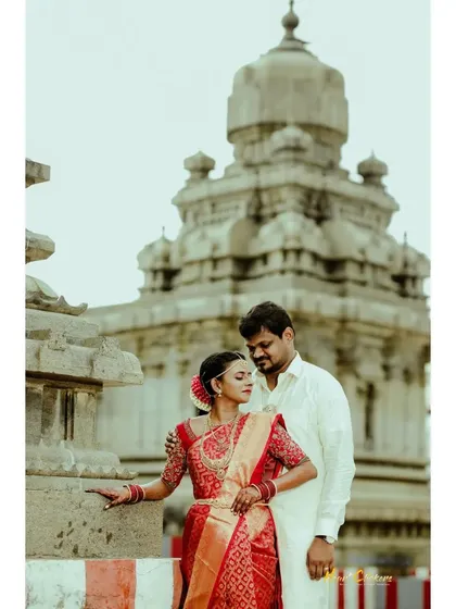 An intimate pose against the backdrop of a temple. The bride's red silk saree and traditional hairstyle are highlighted in this beautiful cultural portrait.