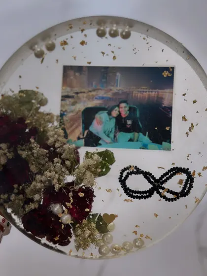 This circular keepsake preserves a couple's photo along with a special infinity bracelet made of black beads. It’s a beautiful way to combine a picture with a tangible object that tells a story.