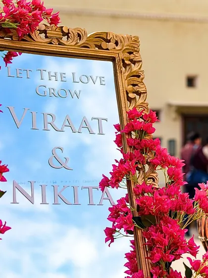 A personalized decor detail for a Mehendi, with the couple's names and a welcome message etched onto a mirror framed with vibrant bougainvillea.