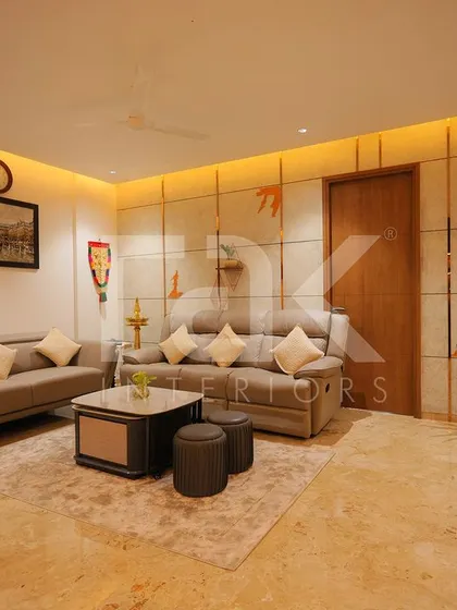 The living room from Dr. Deepak and Dr. Meera's home, featuring neutral-toned sofas, warm ambient lighting, and subtle wall details for a calm atmosphere.