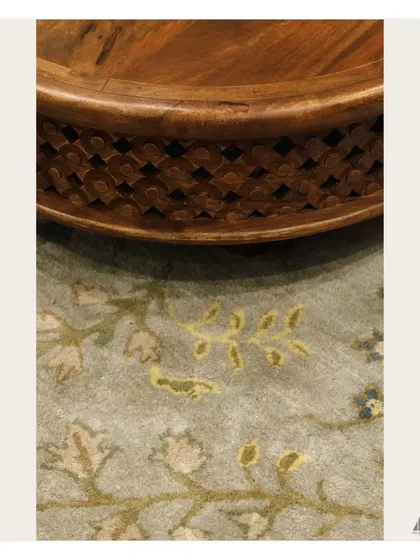 A close-up of the details that define our Indo-Contemporary style. The image highlights the intricate carving on the wooden coffee table set against the soft texture of a floral rug.