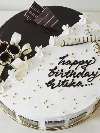 A stylish black and white themed cake with chocolate curls and garnishes, offering a classic and elegant look.