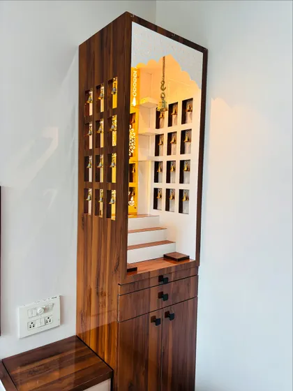 A full view of a standalone wooden mandir. The side panels have small cutouts with bells, and the unit includes drawers and cabinets for storing pooja essentials.