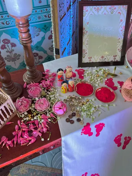 A table of blessings featuring auspicious kumkum footprints, tiny wooden dolls representing the family, and fresh lotus buds.