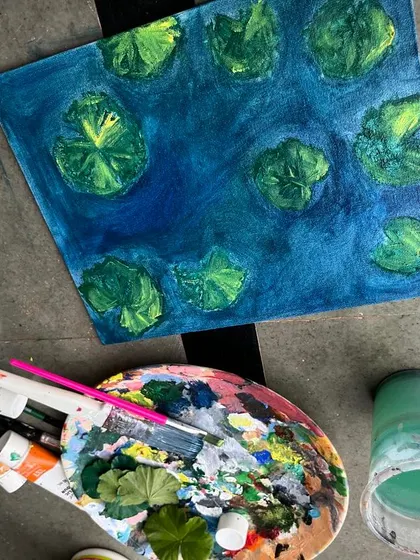 This image shows the work in progress of the koi pond painting. You can see my palette, brushes, and the initial layers of blue and green that form the base of the water scene.