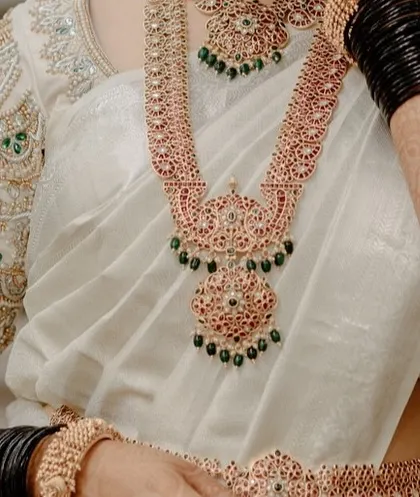 A detailed close-up of a bride's traditional South Indian temple jewelry worn over her white saree. We pay close attention to capturing the craftsmanship of every wedding detail.