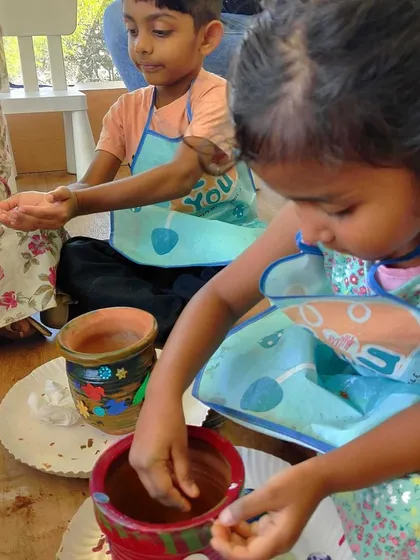 A child decorates her pot with colorful materials. This image shows how we integrate art and creativity into all our activities, even gardening.