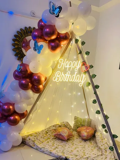 A cozy birthday setup with a canopy tent decorated with balloons and fairy lights.