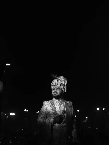 A wide-angle, black and white shot of the groom standing under spotlights, creating a cinematic feel.