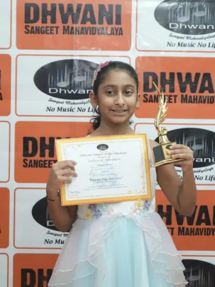 A young performer in her beautiful stage dress, holding her award for her performance.