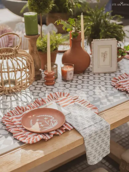 A close-up of the table setting, featuring hand-painted terracotta plates, striped napkins, and rustic candle holders.