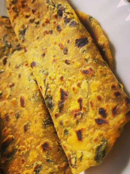 A close-up of the Methi Parathas, showing the specks of green fenugreek leaves and the perfectly cooked, flaky texture.