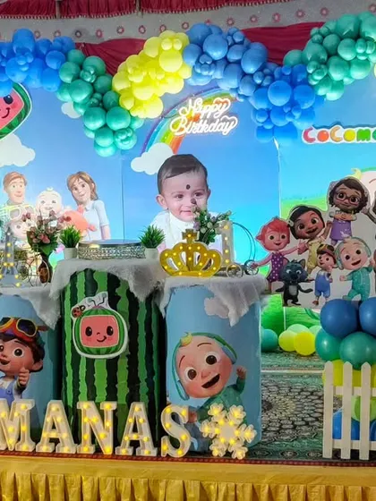 A first birthday party with a Cocomelon theme, featuring a large number '1' prop and character cutouts on a decorated stage.