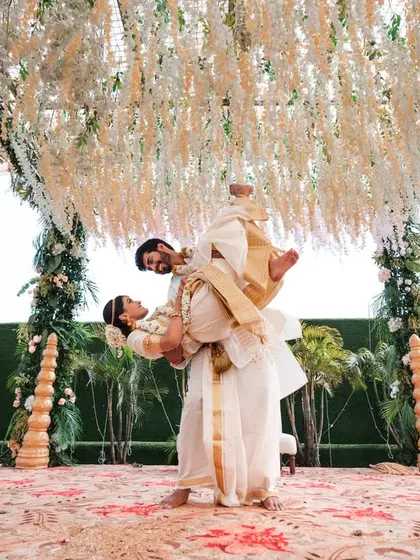 A dramatic and romantic lift, showcasing the bride's traditional white and gold saree against the beautiful mandap.