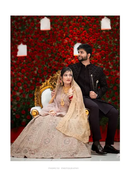 A regal portrait of the couple seated against a stunning wall of red roses, a classic and elegant reception shot.