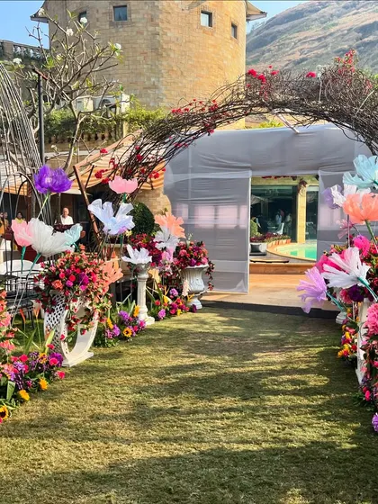 The entrance to the Haldi Carnival, featuring a rustic archway made of branches and adorned with colorful paper flowers, creating a whimsical and inviting entryway.