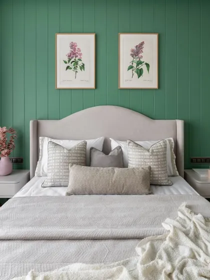 A close-up of the bed in the green-walled room. The mix of textures in the pillows and blanket, along with the simple floral art, adds depth and interest to the serene design.