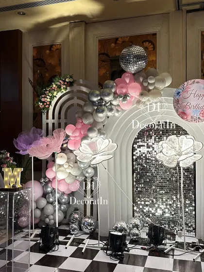 A glamorous disco-themed setup for a 14th birthday. This decor features a silver sequin wall, glowing flower props, and a pink and silver balloon garland, creating a fun and sparkly party vibe.