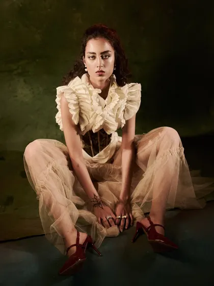 A wide, seated pose that feels both grounded and defiant. The lighting highlights the textures of the tulle and corsetry.