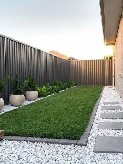 A simple and elegant side yard solution. We used a strip of green lawn, a gravel path with stepping stones, and a row of plants in matching pots to create a clean, low-maintenance space.