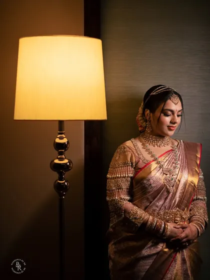 A serene portrait of the bride in her stunning wedding saree, lit by the warm glow of a lamp.
