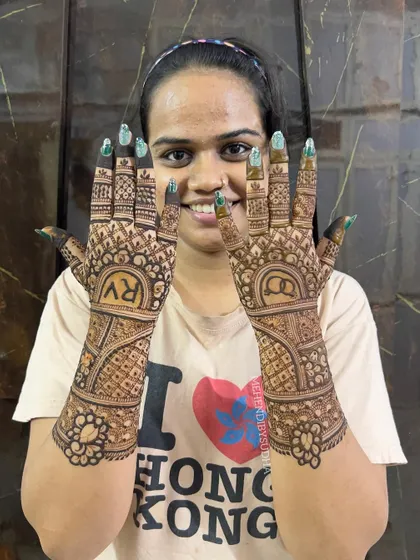 A happy bride-to-be showing her engagement mehendi, personalized with initials 'R' and 'V'.