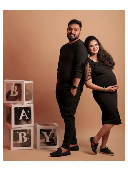 A relaxed pose from a couple's maternity shoot. They are coordinated in black, creating a modern and intimate feel against the neutral backdrop.