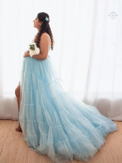 A beautiful silhouette shot by the window, showcasing the long, flowing train of the light blue maternity gown.