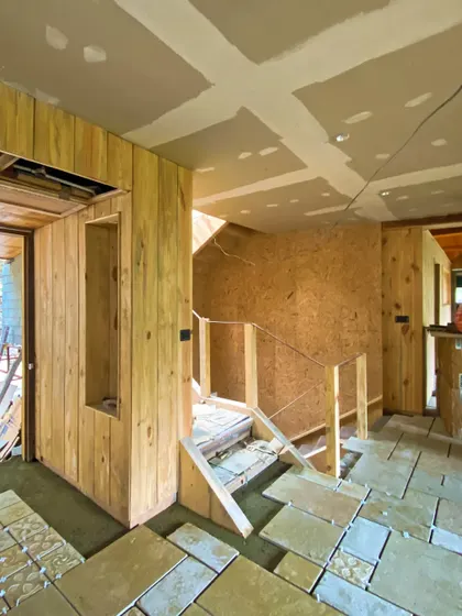 The homestay under construction, showing the process of laying stone floor tiles and installing the wooden wall panels and staircase.