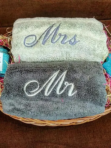 For a minimalist yet elegant gift, this hamper is perfect. It features 'Mr' and 'Mrs' towels in contrasting grey tones, paired with bath salts and a handcrafted soap in a simple wicker basket.