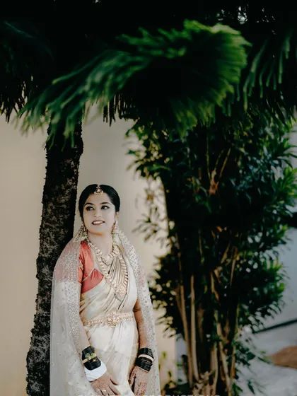 A serene portrait of the bride leaning against a palm tree, capturing a moment of calm before the wedding festivities.