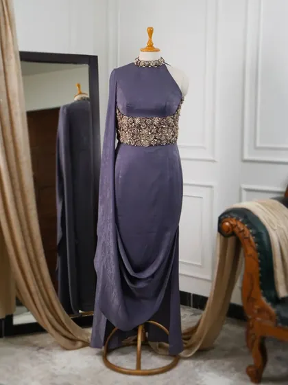 The full view of this one-shoulder gown shows how the corseted waist cinches the silhouette, while the draped skirt and single cape-like sleeve add a touch of drama.