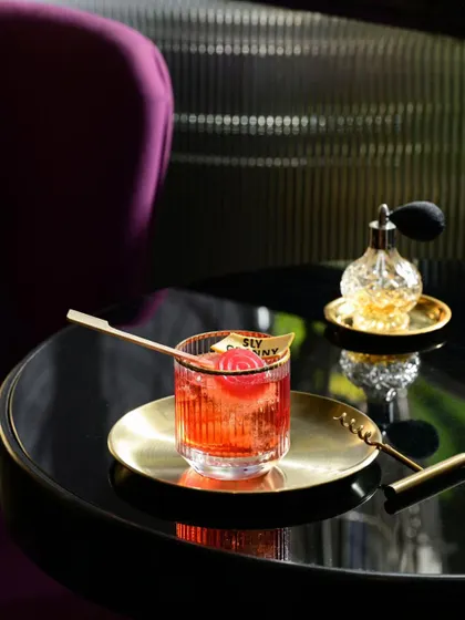 A close up of a cocktail on a table, with the plush purple seating in the background, giving a sense of the luxurious and comfortable ambiance.