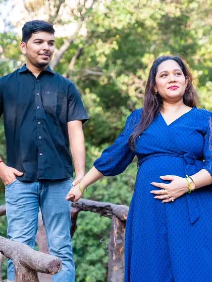 A simple, elegant portrait of an expecting couple on a rustic wooden bridge. The natural setting and their comfortable poses create a feeling of peace and anticipation.