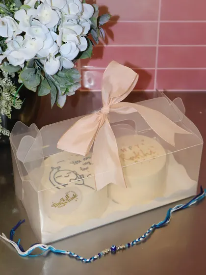 A perfectly packaged Rakhi gift set featuring two custom bento cakes in a clear box with a ribbon. It's a sweet and simple way to send love to your sibling on this special day.