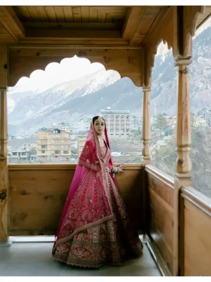 A beautiful bridal portrait on a wooden balcony overlooking Manali. The bride's pink lehenga adds a pop of color to the rustic, scenic backdrop.