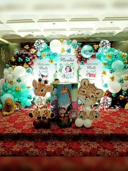 A cute and colorful jungle-themed stage for a combined birthday and twin baby welcome party, featuring adorable cartoon animal cutouts and vibrant balloon arches.